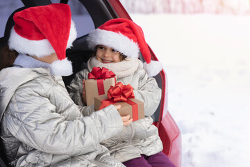 Merry Christmas. Happy Children holds a gift box in the trunk of the car In winter. Winter holidays. Christmas trips, family vacations