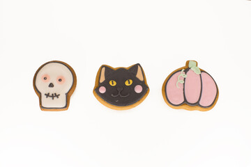 Halloween gingerbread cookies with icing shaped in black cat head, pumpkin and skull in a row of three. Isolated close up shot on a white background