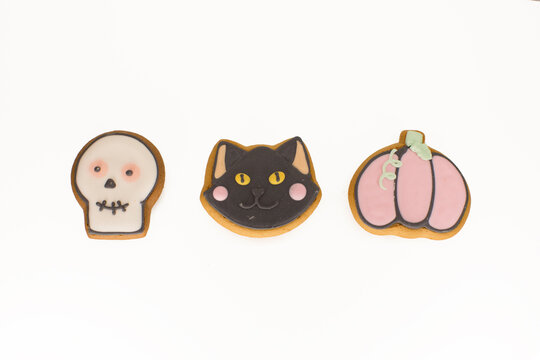Halloween gingerbread cookies with icing shaped in black cat head, pumpkin and skull in a row of three. Isolated close up shot on a white background