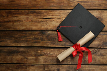 Graduation hat and diploma on wooden table, flat lay. Space for text