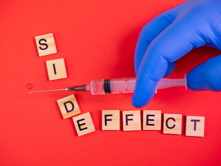 Syringe filled with solution. Words side effect on colored red paper texture background. Concept. Concern of vaccine shot side effect or toxicity. Copy space. Hand blue gloves.