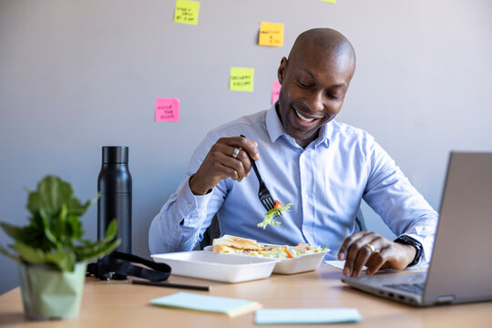 Smiling male entrepreneur having food while sitting at desk in office
