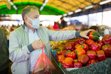 Man in face mask purchasing pepper in greengrocery
