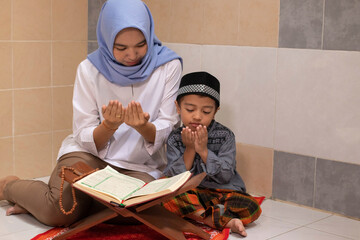 an Asian Muslim mother prays and reads the Al-Qur'an with her son