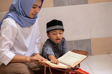an Asian mother is teaching her son to read Al-Qur'an