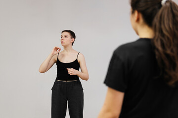 Young speaker woman doing lecture on public. Female actor having a consultation to group of students. Scenic speech exercise. 20 years old coach on stage. Woman with short hair in black top and pants