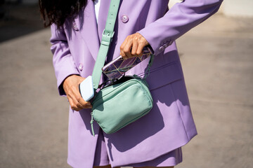 Mid adult woman keeping mobile phone in purse during sunny day