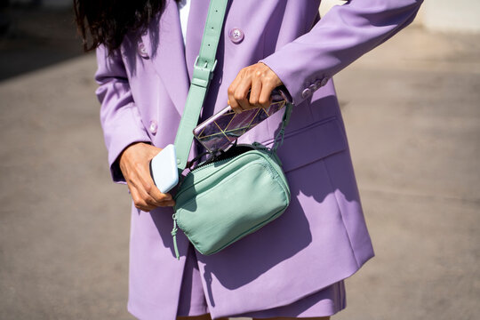 Mid adult woman keeping mobile phone in purse during sunny day