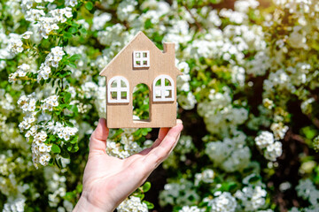 The girl holds the house symbol against the background of white flower
