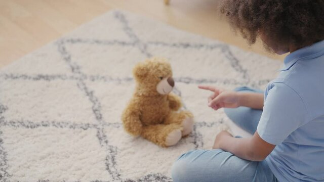 Little girl playing game with teddy bear, scolding toy, copying adult behavior