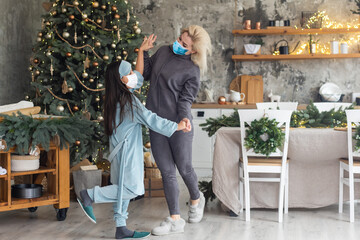 Obraz premium mother and daughter wearing medical masks under the christmas tree during home celebration