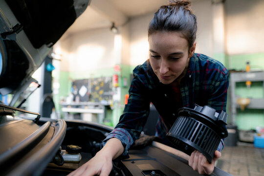 Female mechanic examining car engine at repair shop