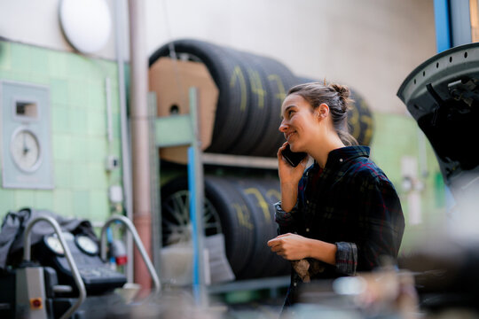 Female mechanic looking away while talking on smart phone at workshop - Powered by Adobe