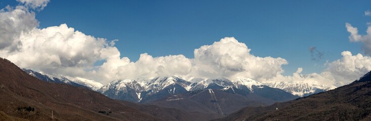 Fototapeta na wymiar Panoramic view of snow capped mountains in the clouds. Caucasian mountains. Sochi Krasnaya Polyana. Russia.