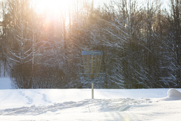 disc golf basket target in sunshine sunset blue snow winter trees forest 