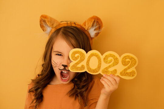 Girl with a painted face in the guise of a tiger growls with her mouth open, holding the number 2022 in hands. New Year of the tiger according to the Eastern calendar. Big discounts, pre-holiday sales