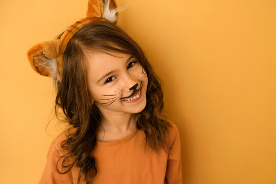 Cute long-haired curly brunette girl with a headband with ears and tiger makeup. Year of the tiger according to the Eastern Chinese calendar.  Symbol of the New Year 2022. Kid in the guise of an anima