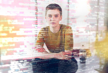 Businesswoman sitting on desk seen through computer codes on glass in office