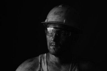 Portrait of a miner wearing a helmet, goggles and a undershirt with a dirty face.