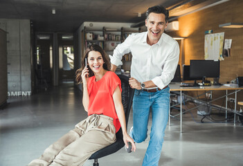 Cheerful colleague spinning businesswoman sitting on office chair
