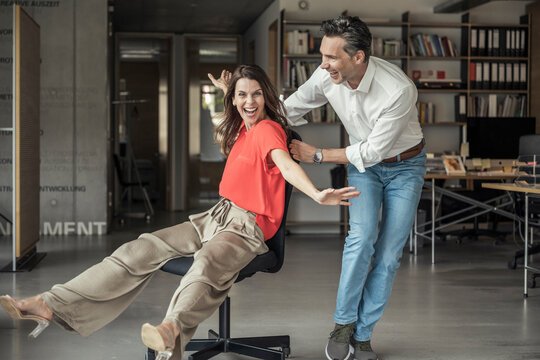 Happy businesswoman playing with colleague while sitting on office chair - Powered by Adobe