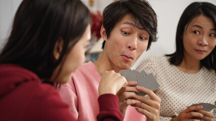 selective focus with closeup of son smiling slyly as the daughter looking at mother's eye gesture and drawing card. playing poker at home during spring festival