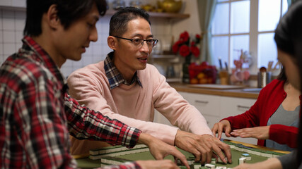 selective focus of father forming the wall of stacks with tiles while playing mahjong with family in the evening at home during spring festival