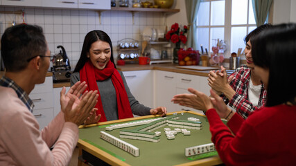 family members clapping hands for the winning daughter who claims a discarded tile and completes her hand while playing mahjong game at home on chinese lunar new year's eve