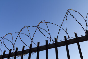 Barbed wire on a high metal fence against the blue sky.