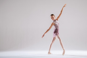 Beautiful young girl ballerina in pointe shoes and pink swimsuit on light background.