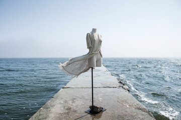 the white headless body of a mannequin are dressed into a summer cape and standing on a pier with...
