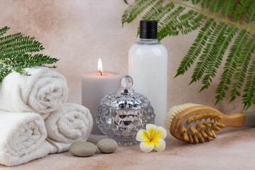 Spa still life treatment composition on massage table in wellness center. Twisted hot towel with aromatic candles and brush on beige background. Aroma therapy setting.