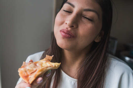 Woman With Eyes Closed Eating Pizza At Home