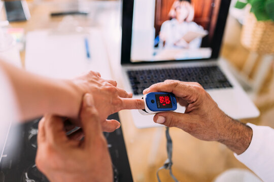 Male doctor examining patient through oximeter during telemedicine in hospital