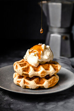 Maple syrup pouring on plate of fresh waffles with ice cream
