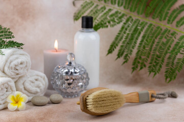 Spa still life treatment composition on massage table in wellness center. Twisted hot towel with aromatic candles and brush on beige background. Aroma therapy setting.