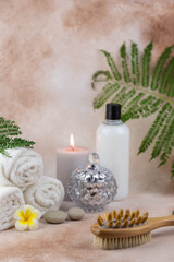 Spa still life treatment composition on massage table in wellness center. Twisted hot towel with aromatic candles and brush on beige background. Aroma therapy setting.