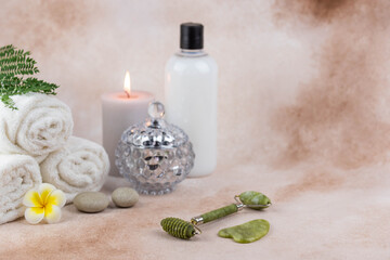Obraz na płótnie Canvas Spa still life treatment composition on massage table in wellness center. Twisted hot towel with aromatic candles and face roller gua sha on beige background. Aroma therapy setting. 