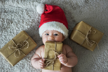 newborn baby in christmas outfit with santa claus hat and eco friendly paper present boxes for xmas...