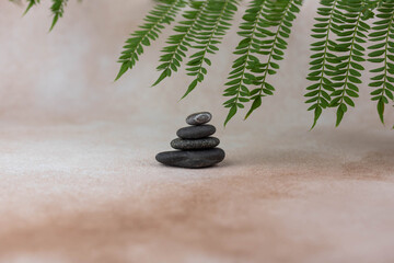 Obraz premium Pyramids of gray zen pebble meditation stones with green leaves on beige background. Concept of harmony, balance and meditation, spa, massage, relax.