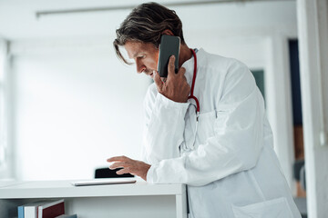Male doctor using digital tablet while talking on smart phone in hospital