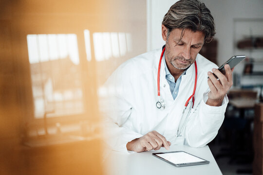 Male healthcare worker using digital tablet while leaning on desk in clinic