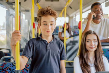 Young school-age boy is riding public transport bus to elementary school holding phone in hand looking out window holding onto railing, waiting for the bus to stop so he can get off © ABCreative