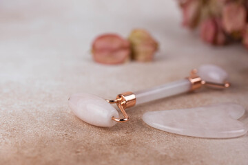Face roller and guasha massager with dry flowers on beige background.