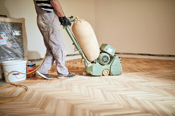 Repairman restoring parquet with a sanding machine. © astrosystem