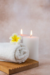 Fototapeta na wymiar Spa still life treatment composition on massage table in wellness center. Twisted hot towel with aromatic candles on beige background. Aroma therapy setting. Concept of harmony, balance and meditation