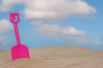 Fototapeta na wymiar Toy Shovel on Sandy Beach With Blue Sky