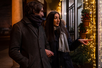 Young couple walking in front of the illuminated shop windows in the evening holding shopping bags