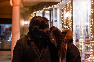 Young couple walking in front of the illuminated shop windows in the evening wearing warm clothes...