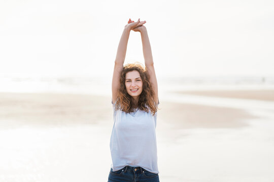 Smiling woman with arms raised standing at beach